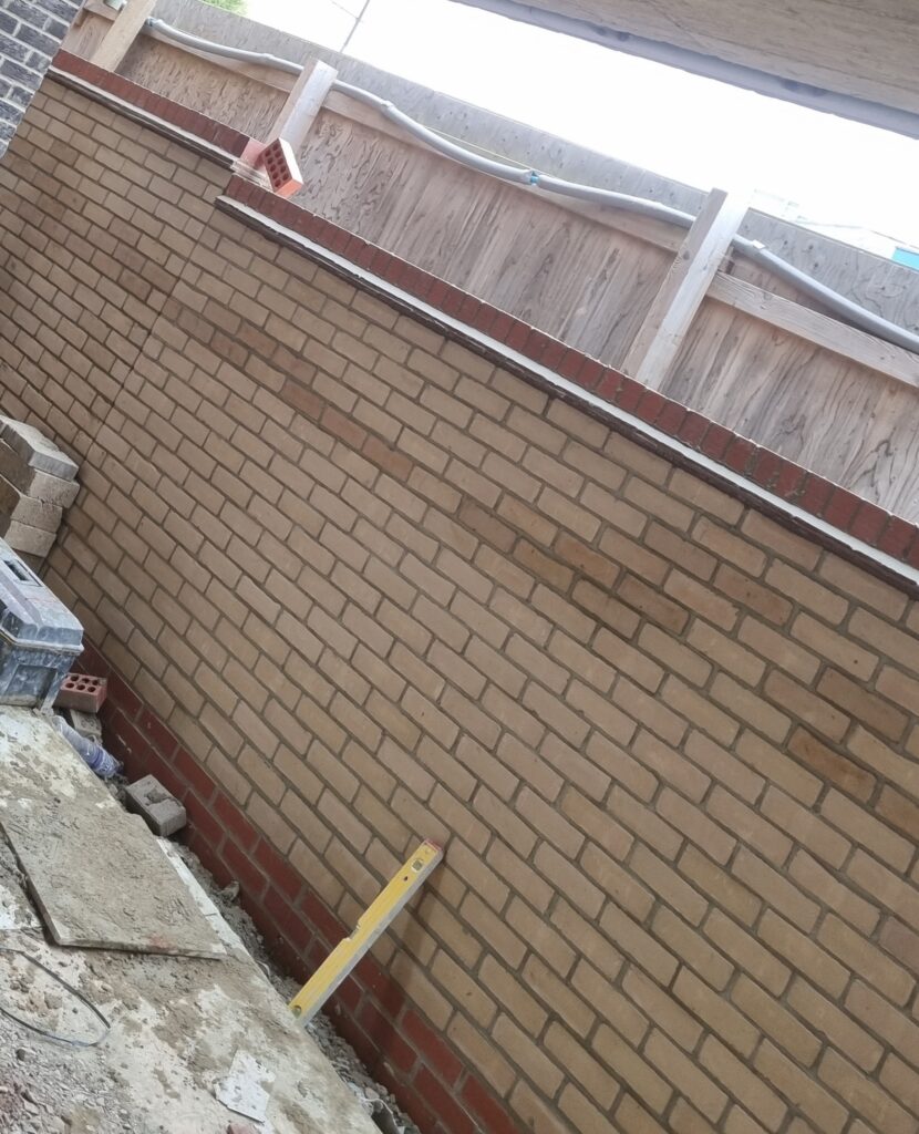 Newly built tan brick wall with dark mortar and red