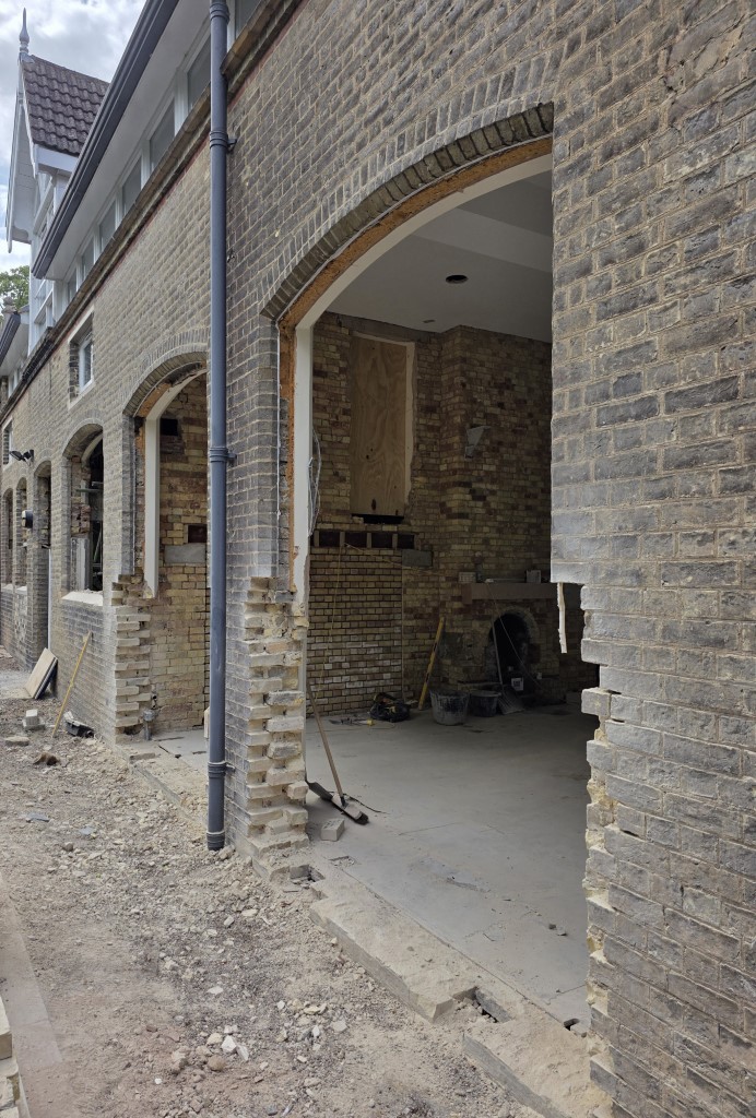 A construction site with a brick building, gray bricks, dirt ground, tools, and an open archway showing a fireplace inside