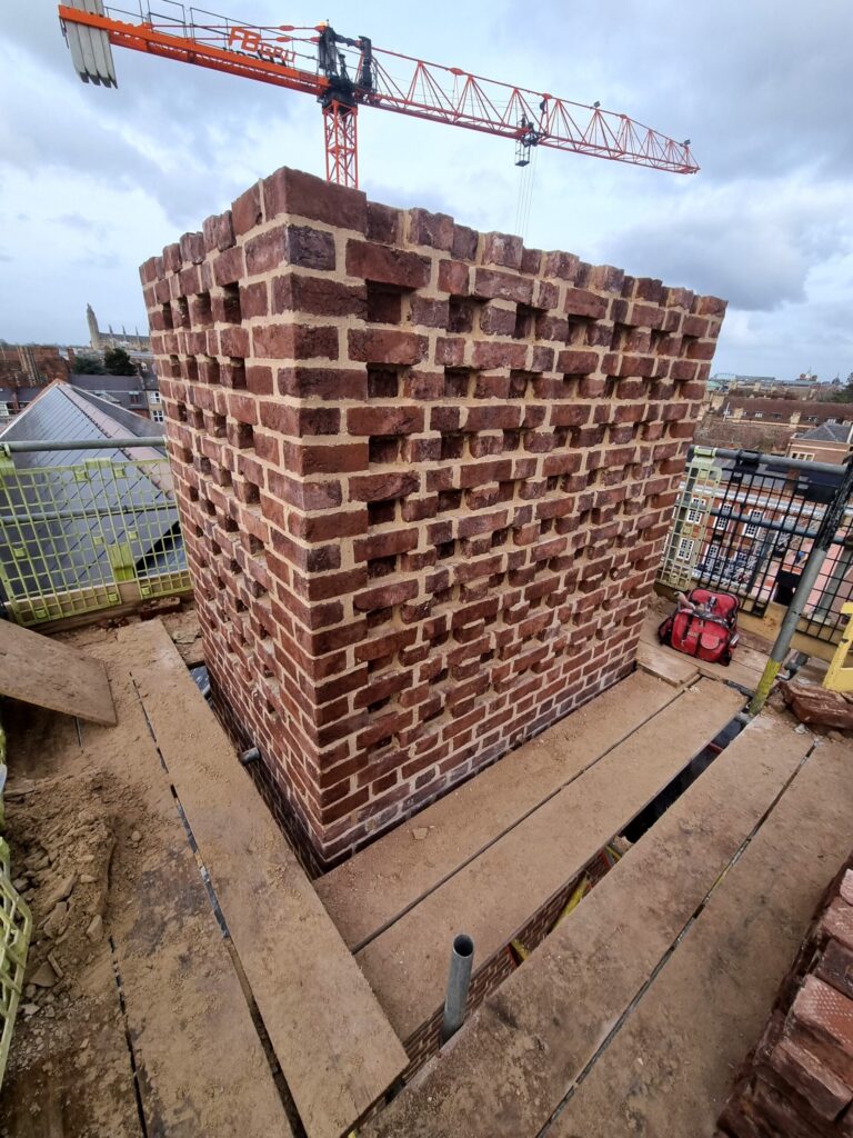 A reddish-brown brick structure with recessed bricks stands on a dusty rooftop