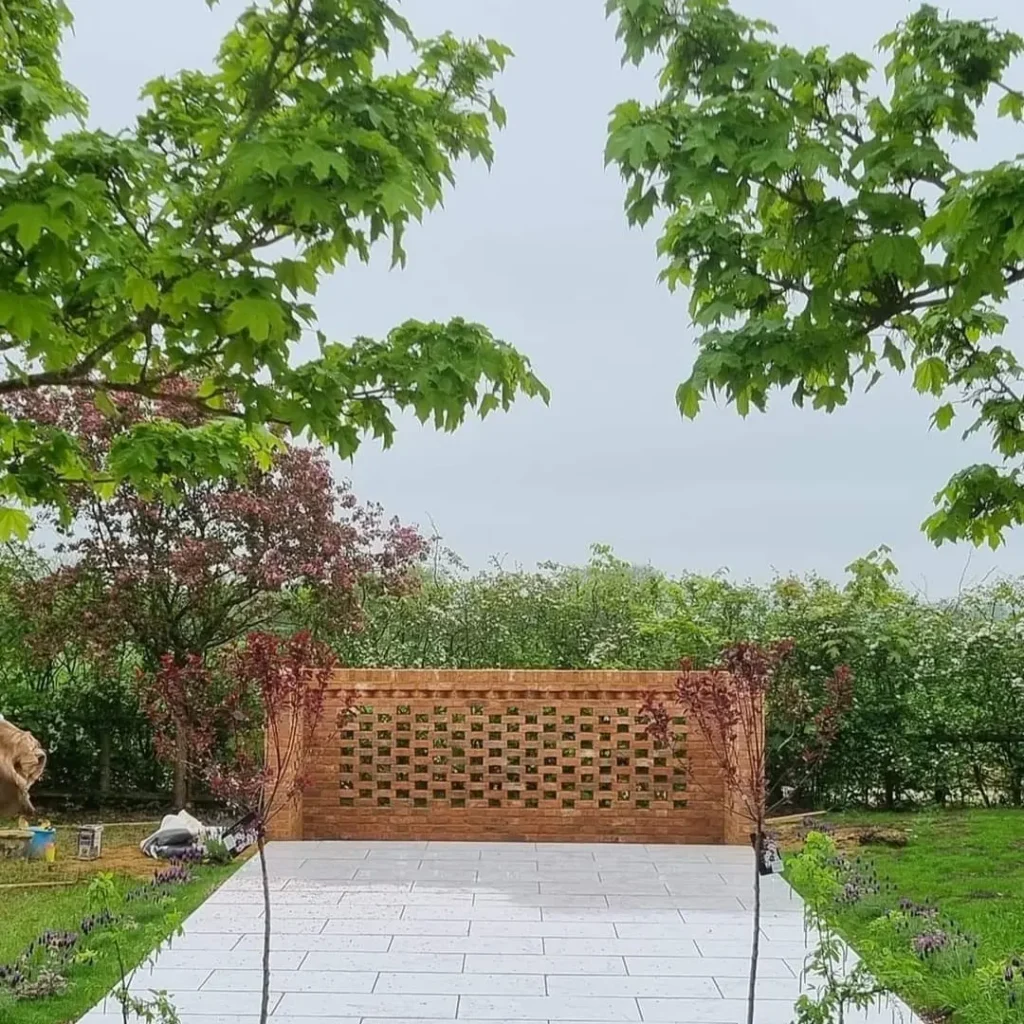 A serene garden path of light grey pavers leads to a decorative red brick