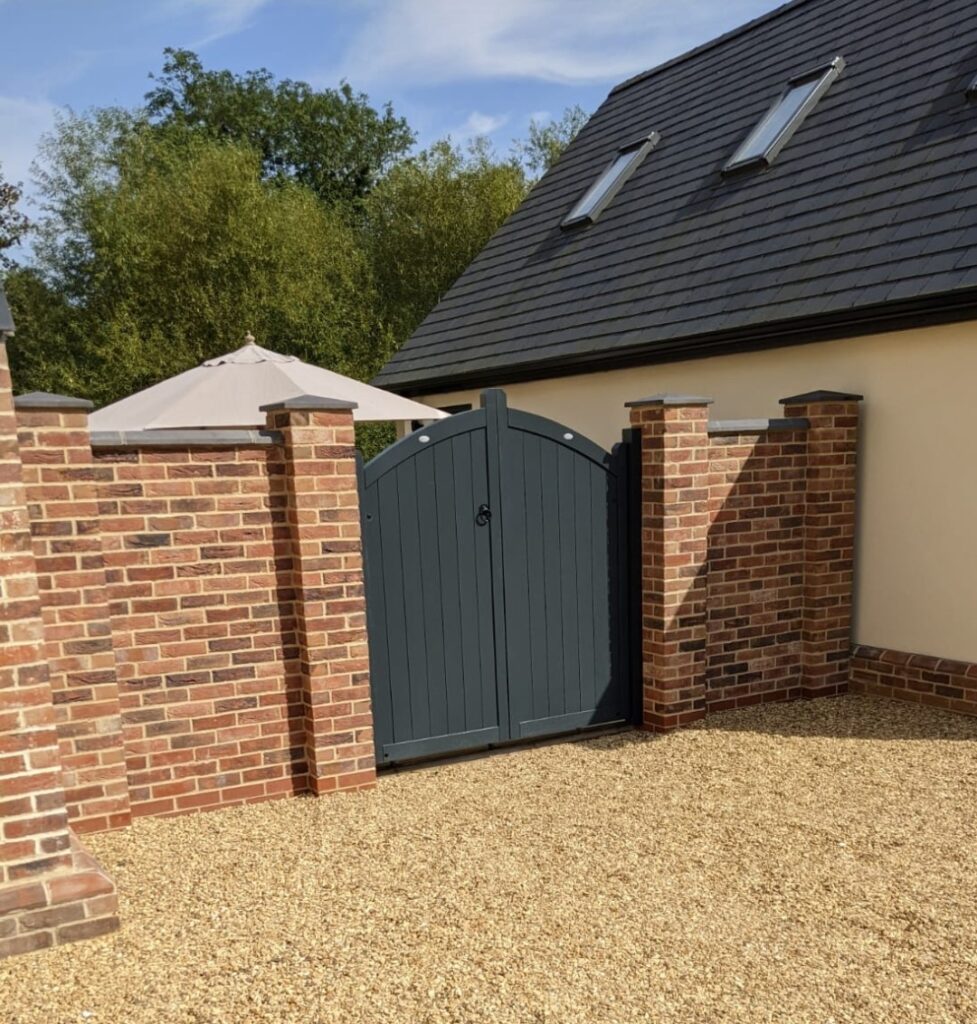 Dark grey wooden arched gate in a red brick wall on