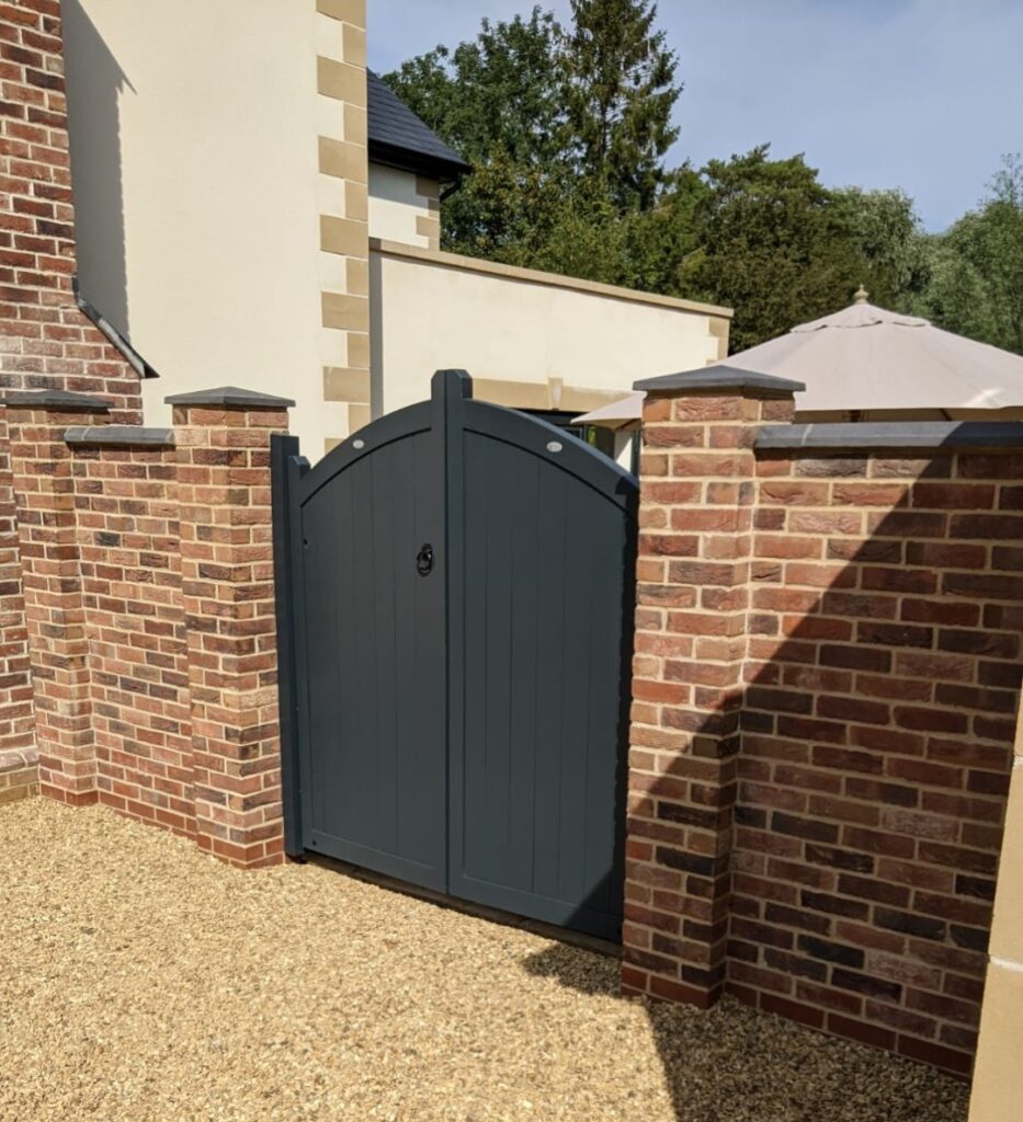 Dark grey arched wooden gate between brick pillars with stone caps,