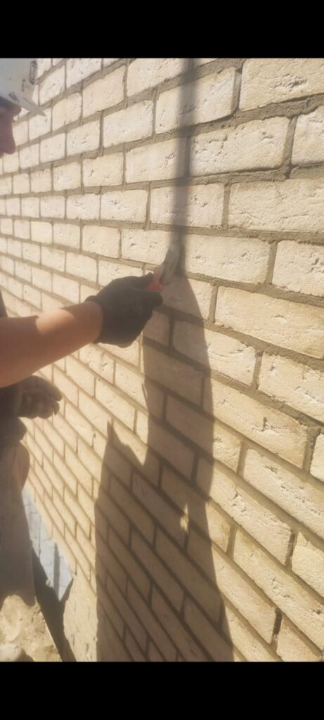 Person in black glove tooling light beige brick wall mortar